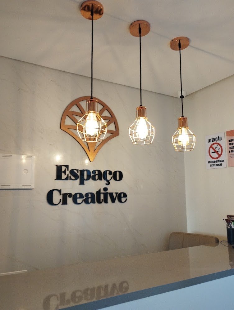 Recepção do Espaço Creative com a marca na parede e pendentes de cobre acesos